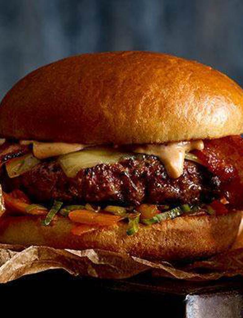 A Korean inspired Kimchi Burger, topped with kimchi, bacon and american cheese, with a gochujang sauce on the gourmet brioche bun, served with hand cut french fries. 