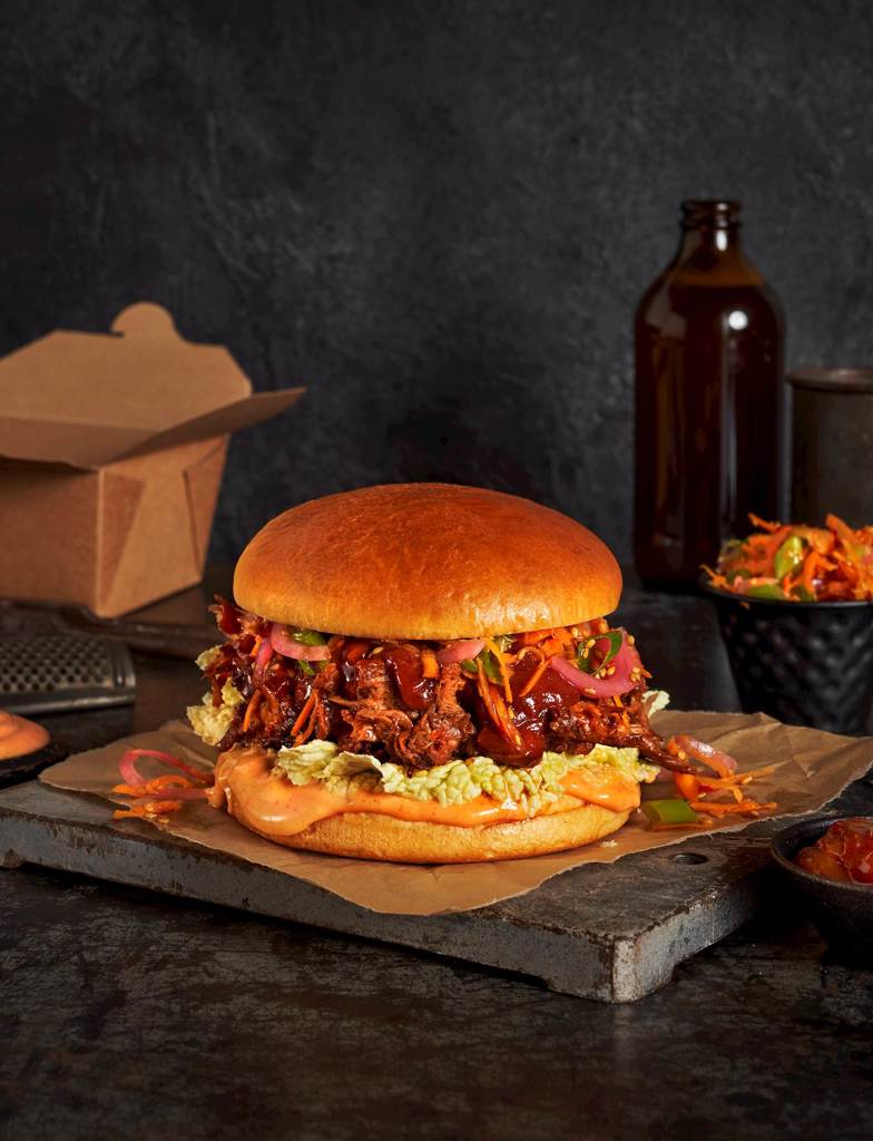 An artful display of An Americana Brioche bun filled with Chinese pulled pork, gochujang mayo, hoisin ketchup and asian slaw.