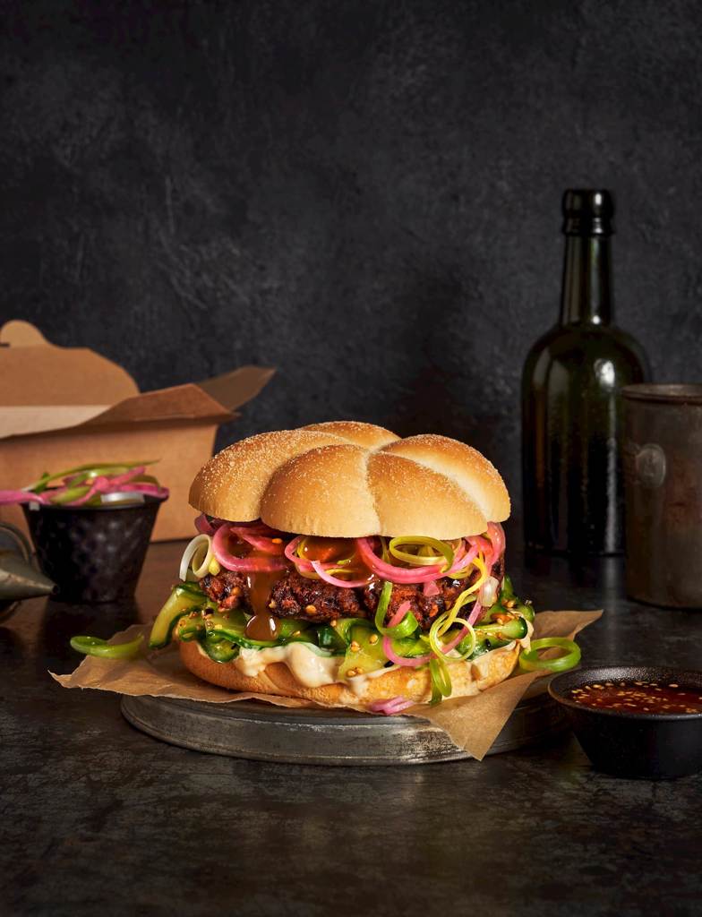 A professional display of a Japanese Teriyaki black bean burger with pickled red onions, miso mayo and cucumber salad stacked in an Americana Gourmet Bun