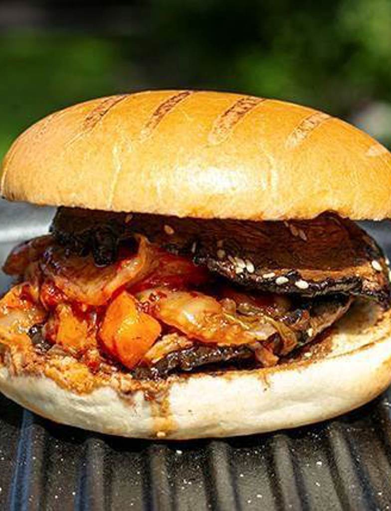 Vegan Americana Grill Marked Brioche Style Bun filled with soy glazed portobello grilled mushrooms, kimchi, and toasted sesame seeds,  on display outside in the sun